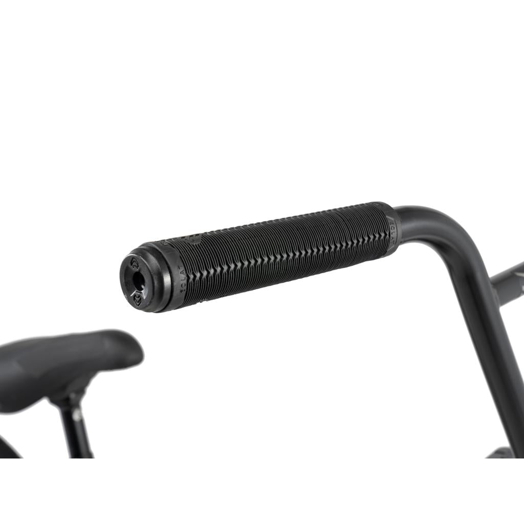 Close-up view of a black rubber handlebar grip attached to the metal handlebar of the Wethepeople 20 inch Envy Carbonic LTD Bike, with part of the bicycle seat visible in the background.