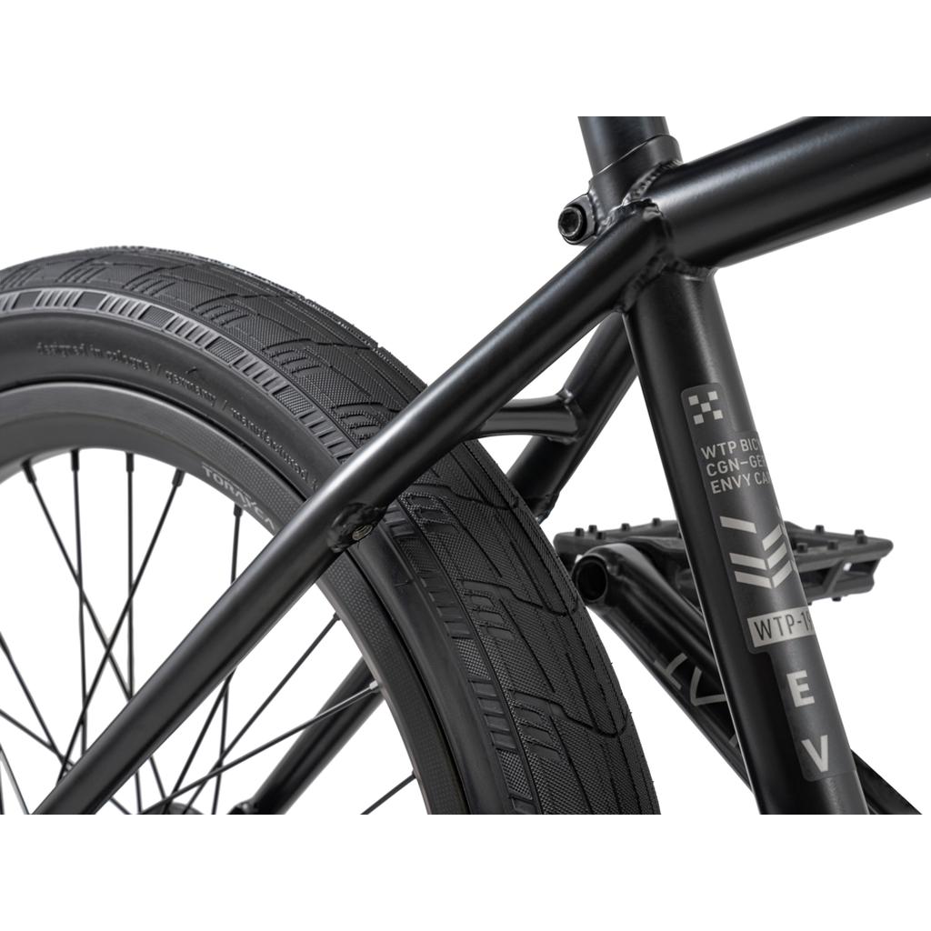 Close-up of the rear wheel, tire, frame, and pedal of a Wethepeople 20 inch Envy Carbonic LTD Bike with visible text and logos on the frame.