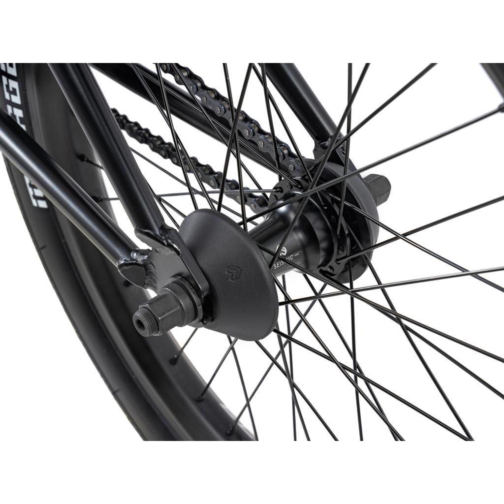 Close-up view of the Wethepeople 20 inch Envy Carbonic LTD Bike’s rear wheel hub, featuring the axle, spokes, chain, and a protective hub guard.
