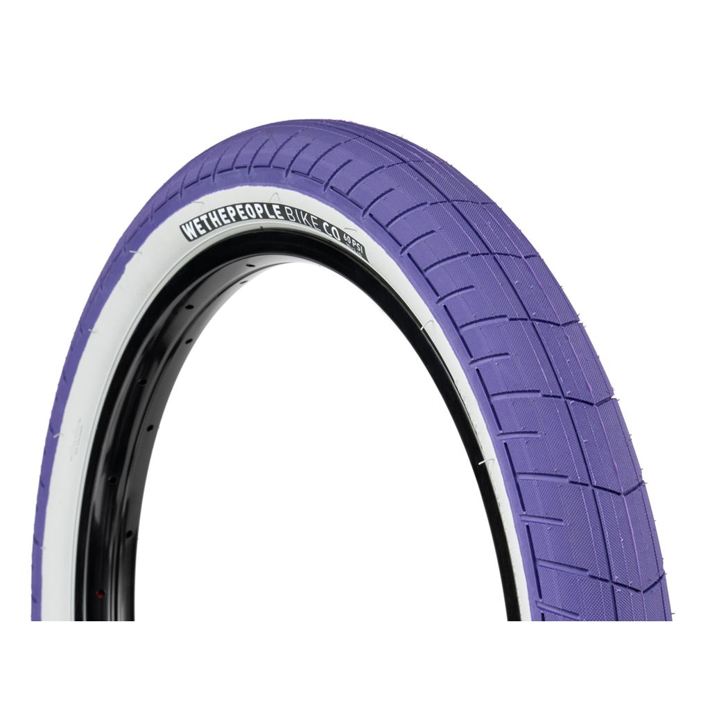 The Wethepeople Activate Tyre (60 PSI) is a purple bicycle tire with a white wall and visible tread pattern, featuring the "WeThePeople Bike Co." logo on the side. This high-pressure tire includes a nylon-reinforced sidewall for enhanced durability and performance, making it ideal for cyclists looking to kickstart their adventures.