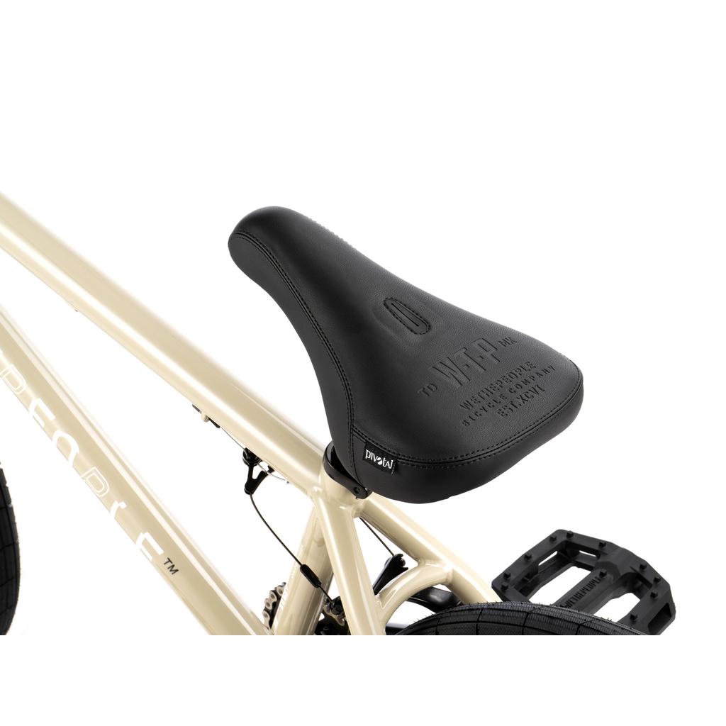 Close-up of a black Salt Comp seat with embossed text, attached to the cream-colored Wethepeople Arcade 20 Inch Bike—ideal for any mid-tier setup.