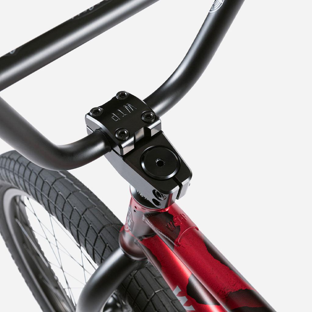 Close-up of the Wethepeople Audio 22 Inch Bike's handlebar and front wheel, highlighting the black stem and red frame detailing against a sturdy chromoly frame.