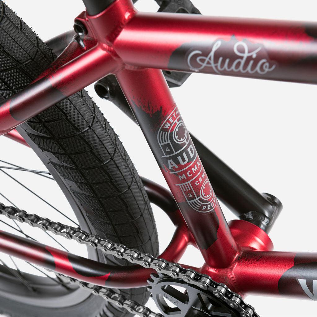 Close-up of a Wethepeople Audio 22 Inch Bike in red, showcasing the chain, tire, and detailed graphics on the sturdy chromoly frame.
