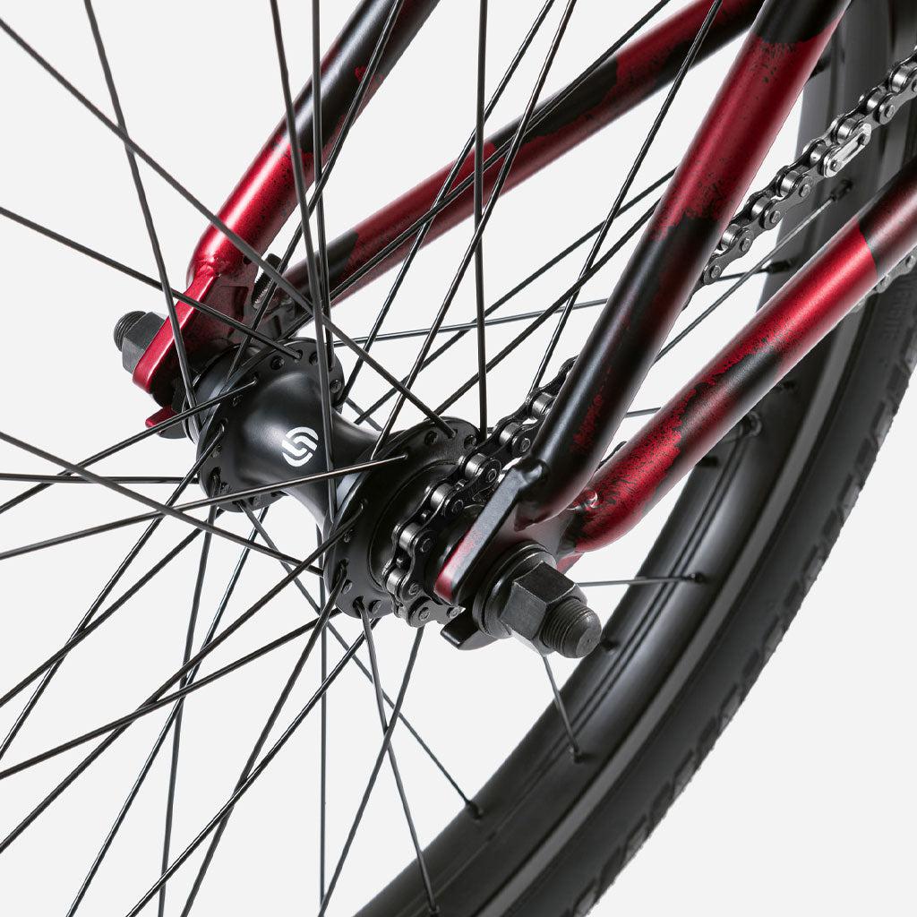 Close-up of the Wethepeople Audio 22 Inch Bike wheel, highlighting the hub, spokes, and chain in a striking red and black color scheme.