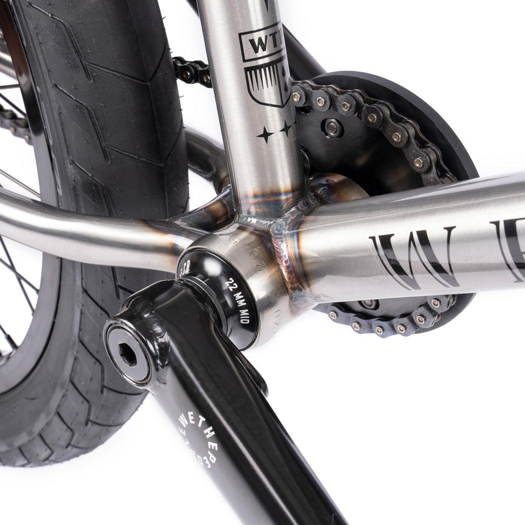 Close-up of the Wethepeople Battleship 20 Inch Bike’s rear wheel, crank arm, and chain, showcasing Chromoly frame welds and gear details against a white background.