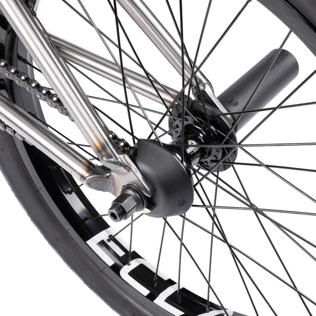 Close-up of a rear wheel on the Wethepeople Battleship 20 Inch Bike, featuring metal spokes, black hub, axle nut, chain, and a plastic peg on the axle highlighting quality Eclat components.