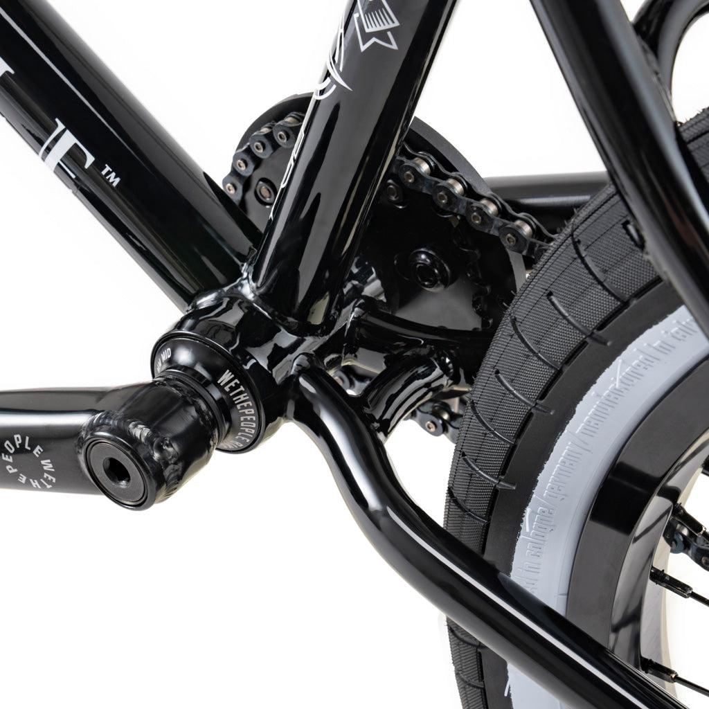 Close-up of the Wethepeople Battleship 20 Inch Bike's black rear wheel, chain, and crank arm, highlighting detailed connection points and tire tread against a white background.