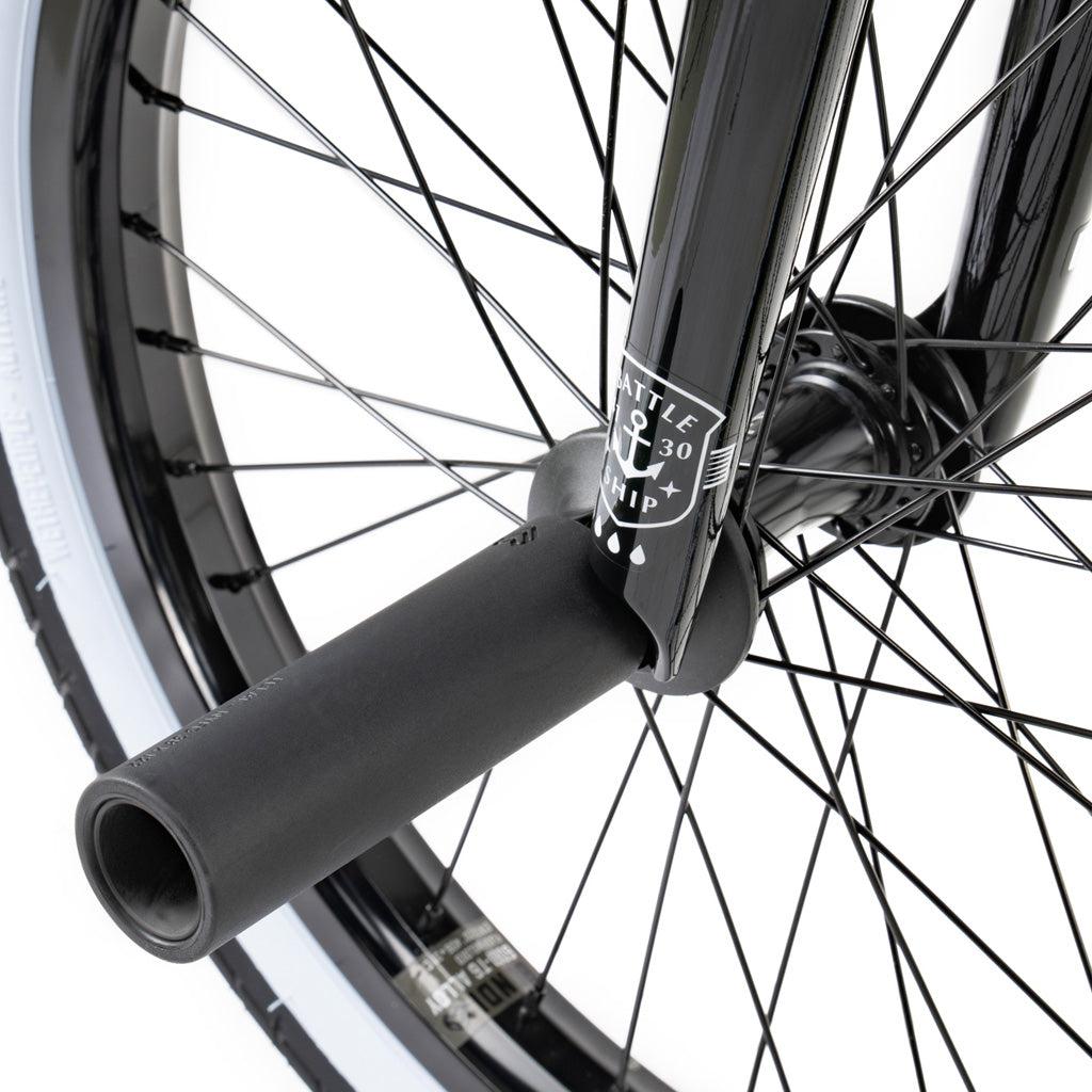 Close-up of the Wethepeople Battleship 20 Inch Bike’s black BMX front wheel, showing spokes, tire, fork, and a mounted axle peg for tricks, featuring durable Eclat components.
