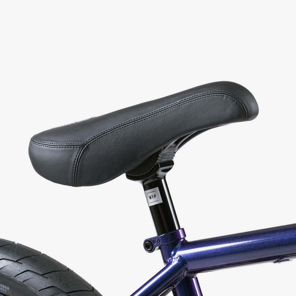 Close-up of a black seat on the Wethepeople Battleship 20 Inch Bike's metallic blue frame, with part of the rear wheel visible against a plain white background.