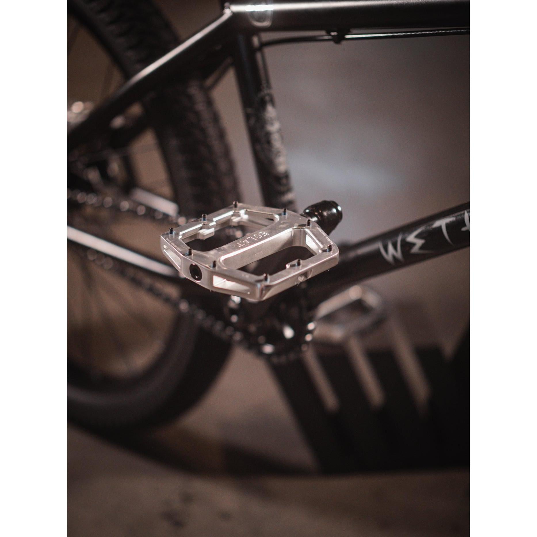 Close-up of a bike pedal attached to a sleek black Wethepeople Chaos Machine 22 Inch Custom Bike frame.