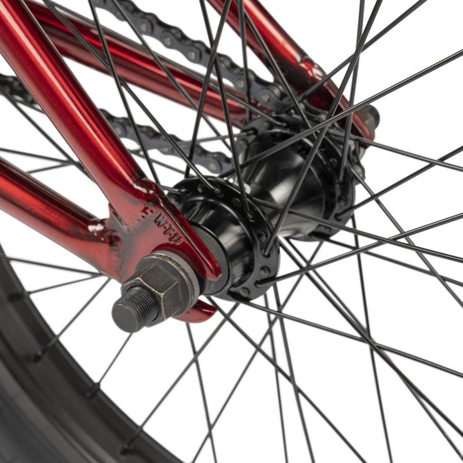 Close-up of the rear wheel on a Wethepeople CRS 18 Inch Bike, featuring the red frame, black hub, axle bolt, spokes, chain, and 18-inch tire.