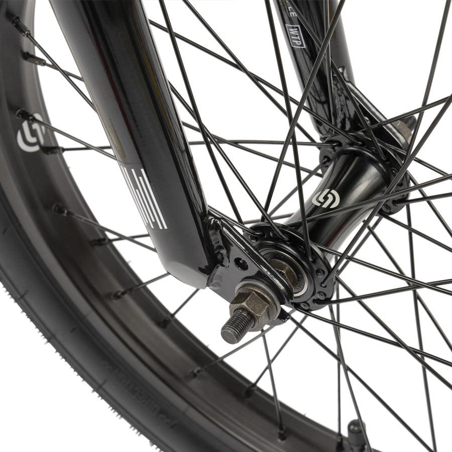 Close-up of the Wethepeople CRS 18 Inch Bike’s black wheel, highlighting its spokes, tire, axle, and fork with visible branding.