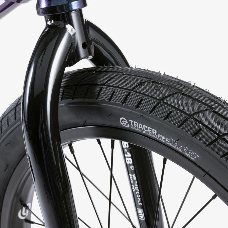 Close-up of the front wheel on a Wethepeople CRS 18 Inch Bike, highlighting the Tracer tire tread, spokes, and fork. The tire brand and size are visible on the sidewall of this kids BMX bike.