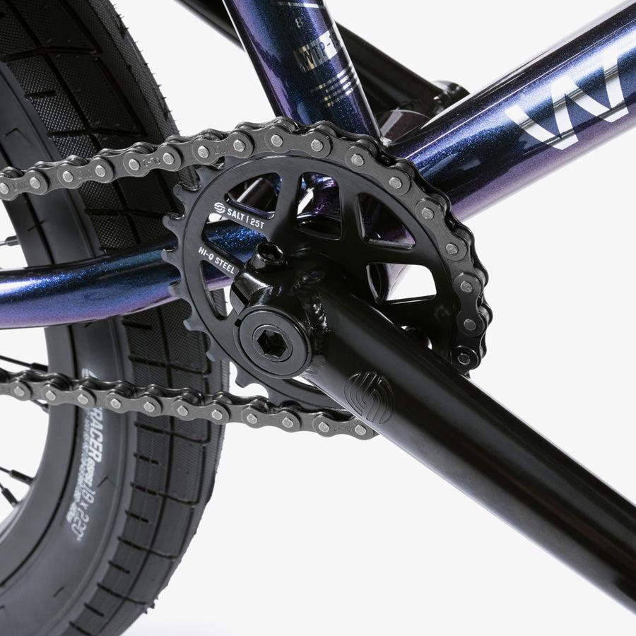 Close-up of the Wethepeople CRS 18 Inch Bike crankset and chainring mounted on a purple kids BMX frame, with part of the rear wheel and tire in view.