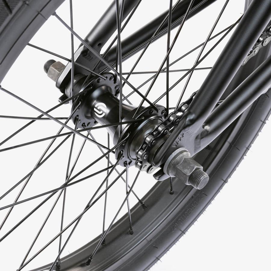 Close-up of a black rear wheel from the Wethepeople CRS 18 Inch Bike, showing spokes, axle, chain, and hub on a white background—perfect for 18 inch BMX or kids BMX bike riders.