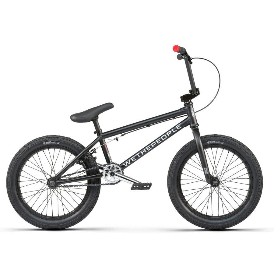 The Wethepeople CRS 18 Inch Bike is shown in side profile, featuring a black frame with "WETHEPEOPLE" branding, 18-inch black wheels, a padded seat, and red handlebar end plugs.