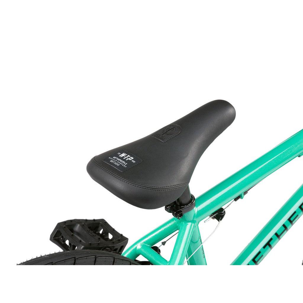 Close-up of a black seat on the Wethepeople CRS FS 18 Inch Bike, showing its teal BMX freestyle frame with rear wheel and pedal partially visible.