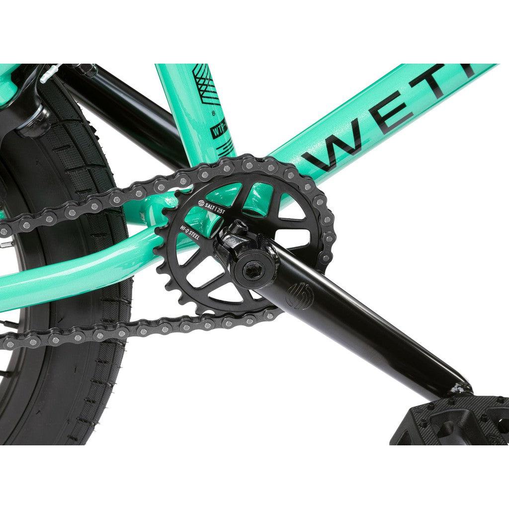 Close-up of the Wethepeople CRS FS 18 Inch Bike in turquoise, highlighting its BMX freestyle frame, chain, chainring, crank arm, and rear wheel tire.