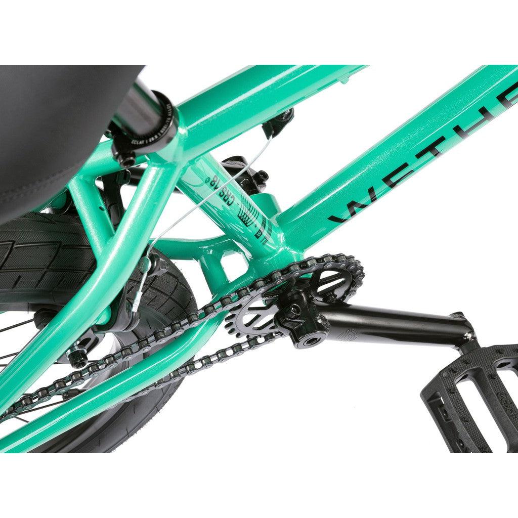 Close-up view of the Wethepeople CRS FS 18 Inch Bike in teal, showing the BMX freestyle frame, chain, crankset, rear wheel, and part of the pedal. The brand name is partially visible on the frame.