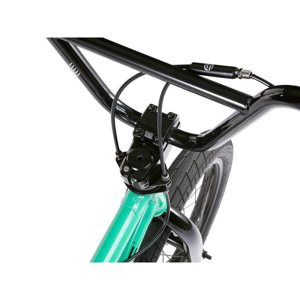 Close-up view of the Wethepeople CRS FS 18 Inch Bike’s handlebars, brake cables, and front wheel with a turquoise fork and sturdy black parts—perfect for BMX freestyle riding.