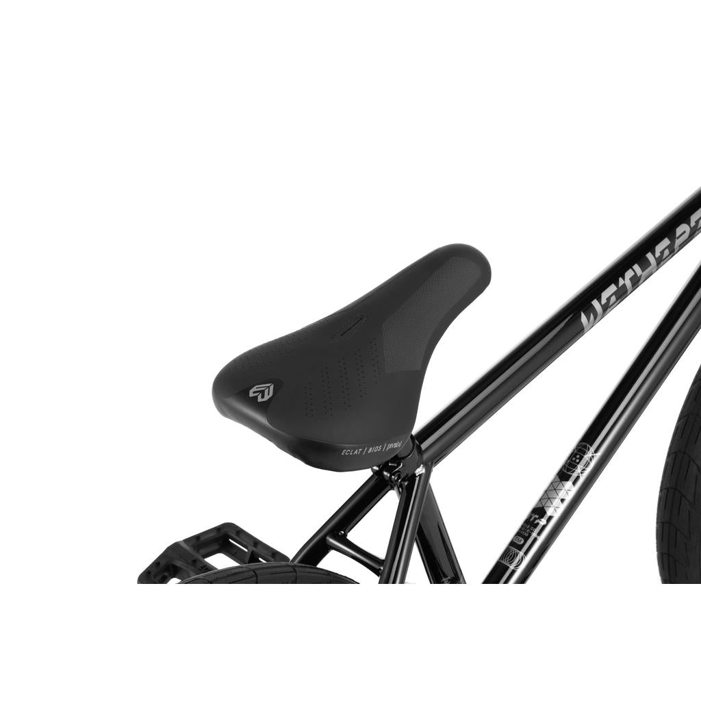 Close-up of a black bicycle seat attached to a black frame, showing part of the rear wheel and pedal on a Wethepeople Envy 20 Inch Bike with premium Eclat parts.