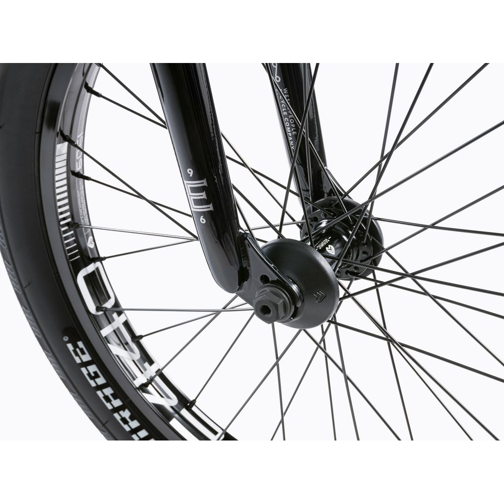 Close-up of the front wheel of a Wethepeople Envy 20 Inch Bike, highlighting black spokes, a sleek black fork, and tire branding.