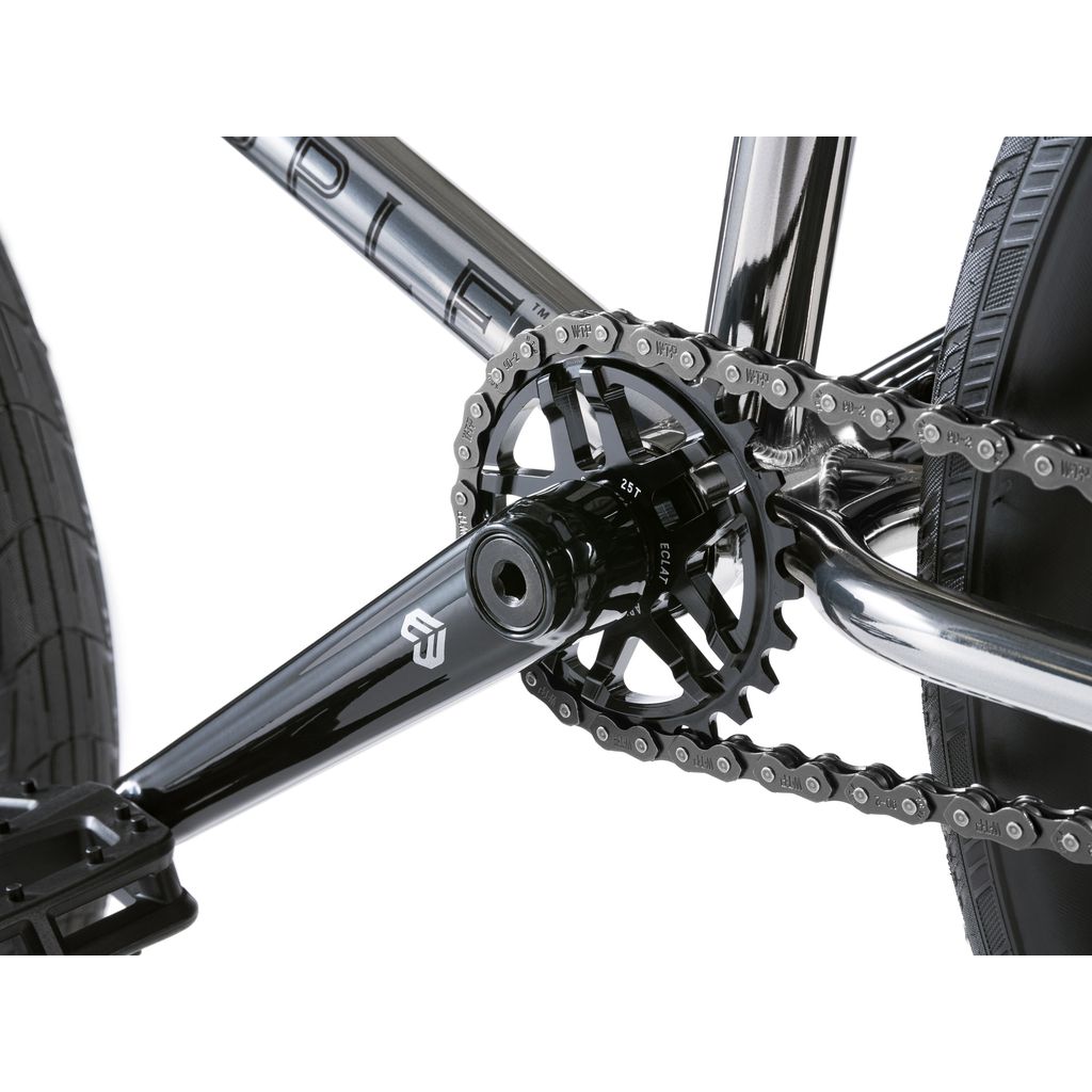 Close-up of a bicycle's black crankset and chain, highlighting the Eclat Tibia Cranks. The frame of the Wethepeople Envy 20 Inch Bike features an embossed logo, with a glimpse of the rear tire—truly a BMX masterpiece.