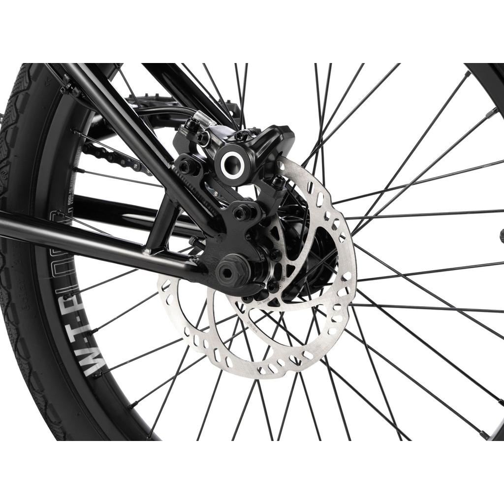 Close-up of the Wethepeople Havoc 20 Inch Bike’s rear wheel features a hydraulic disc brake rotor, caliper, black spokes, and a tire labeled "WTB.