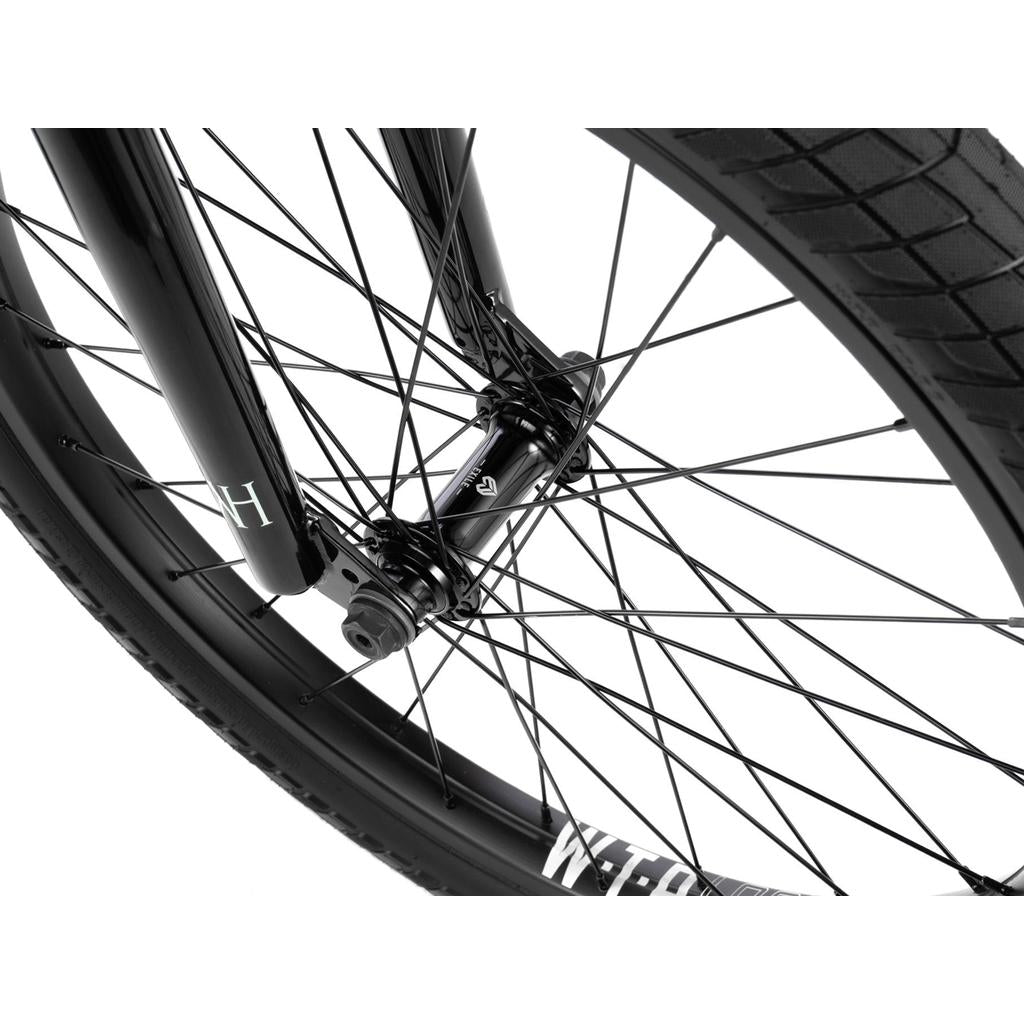Close-up of the front wheel on a Wethepeople Havoc 22 Inch Bike, highlighting black spokes, tire tread, and part of the disc brake-ready fork against a white background.