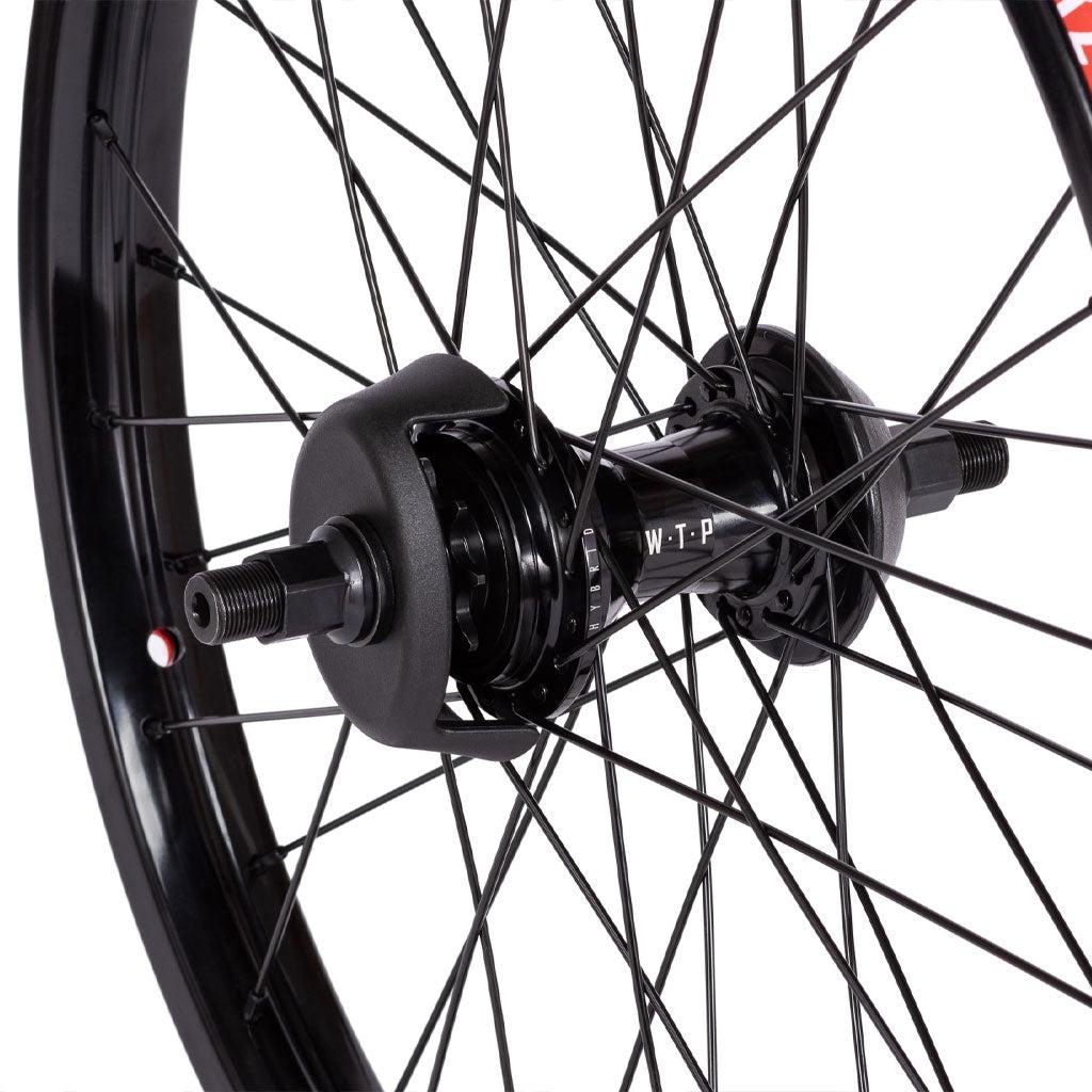Close-up of a black bicycle wheel hub with spokes arranged in a radial pattern, labeled "WTP" on the hub, showcasing the precision engineering of the Wethepeople Hybrid Freecoaster Wheel.
