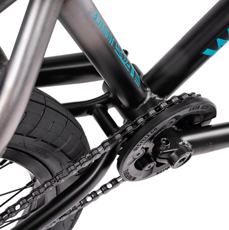 Close-up of the top-of-the-line BMX components and gear mechanism on a Wethepeople Justice 20 Inch Bike's black and metallic frame. The tire and part of the wheel are also visible.
