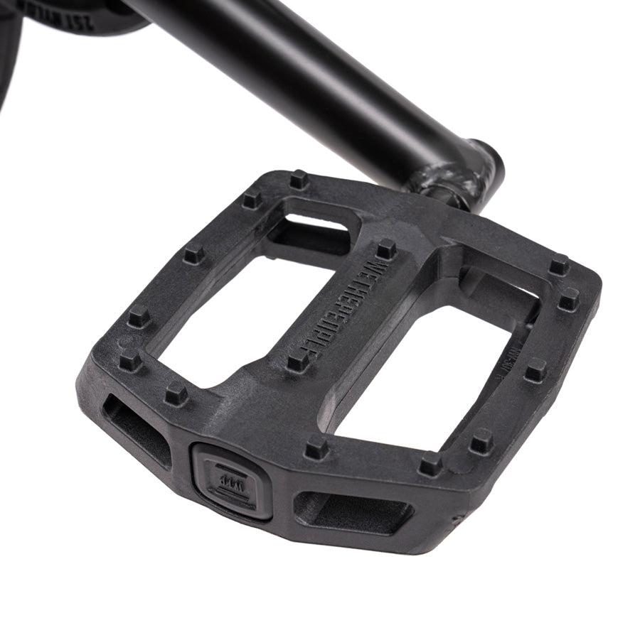 Close-up view of a black bicycle pedal with an open, rectangular design and visible brand markings, attached to the pedal arm of a Wethepeople Justice 20 Inch Bike.