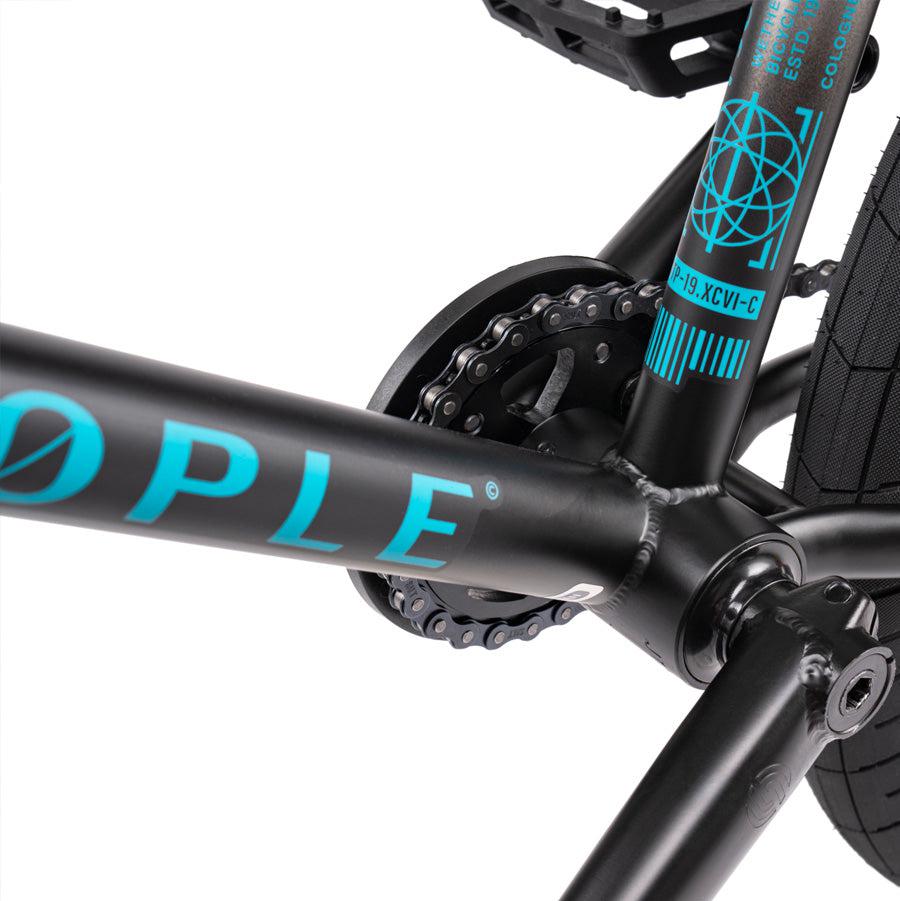 Close-up view of the Wethepeople Justice 20 Inch Bike's black frame with teal blue decals, featuring a detailed focus on the top-of-the-line crankset and chain area.