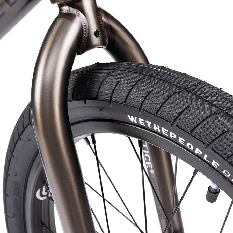 Close-up of the front wheel and tire of the Wethepeople Justice 20 Inch Bike, showcasing the "WETHEPEOPLE" branding on the tire and a metallic bicycle fork. This bike features top-of-the-line BMX components for peak performance.