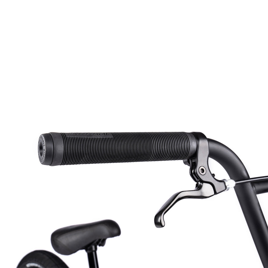 Close-up of the Wethepeople Justice 20 Inch Bike's handlebar and brake lever, featuring top-of-the-line BMX components. A glimpse of the seat and back tire is slightly visible in the background, highlighting its urban style.