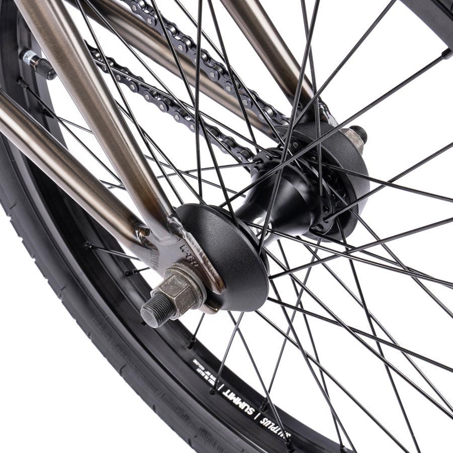 Close-up of a bicycle rear wheel, showcasing the top-of-the-line BMX components including spokes, tire, chain, and axle nuts from the Wethepeople Justice 20 Inch Bike.
