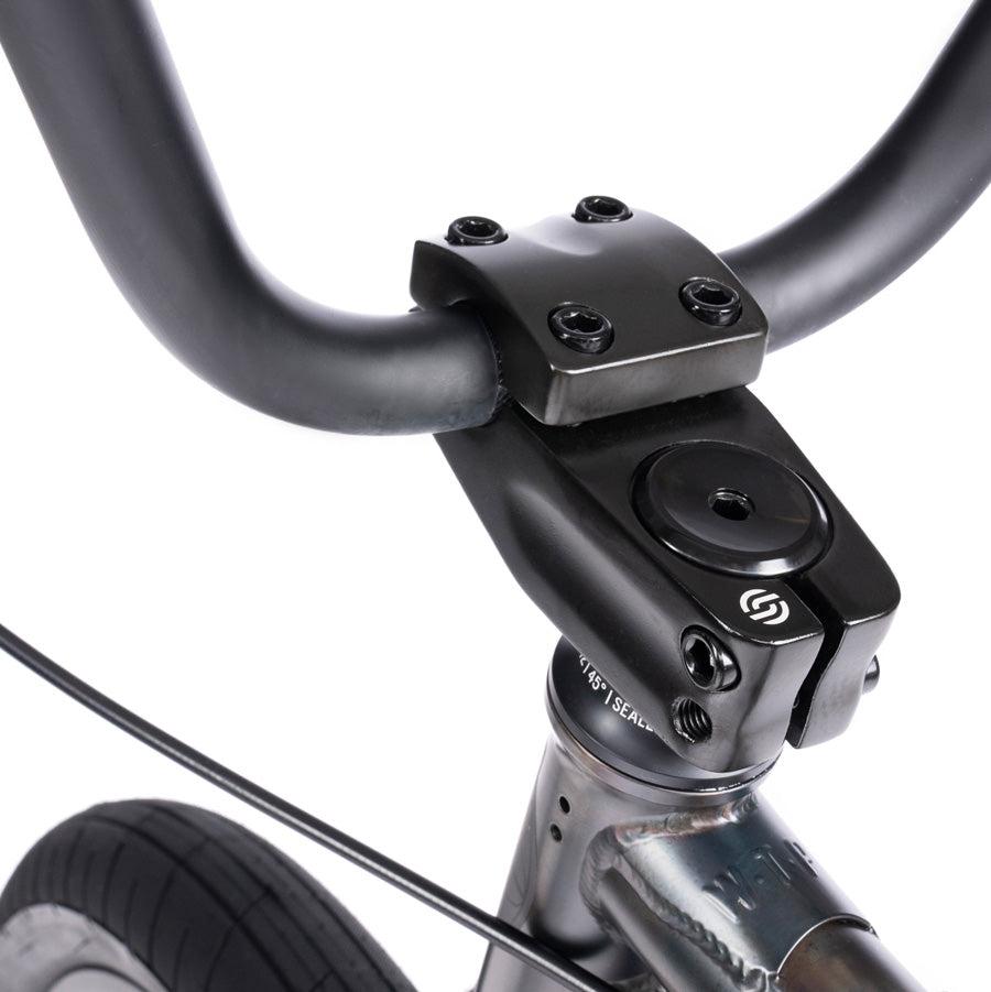 Close-up view of the black handlebar and stem of the Wethepeople Justice 20 Inch Bike, highlighting the bolts and clamp mechanism characteristic of an urban BMX bike.
