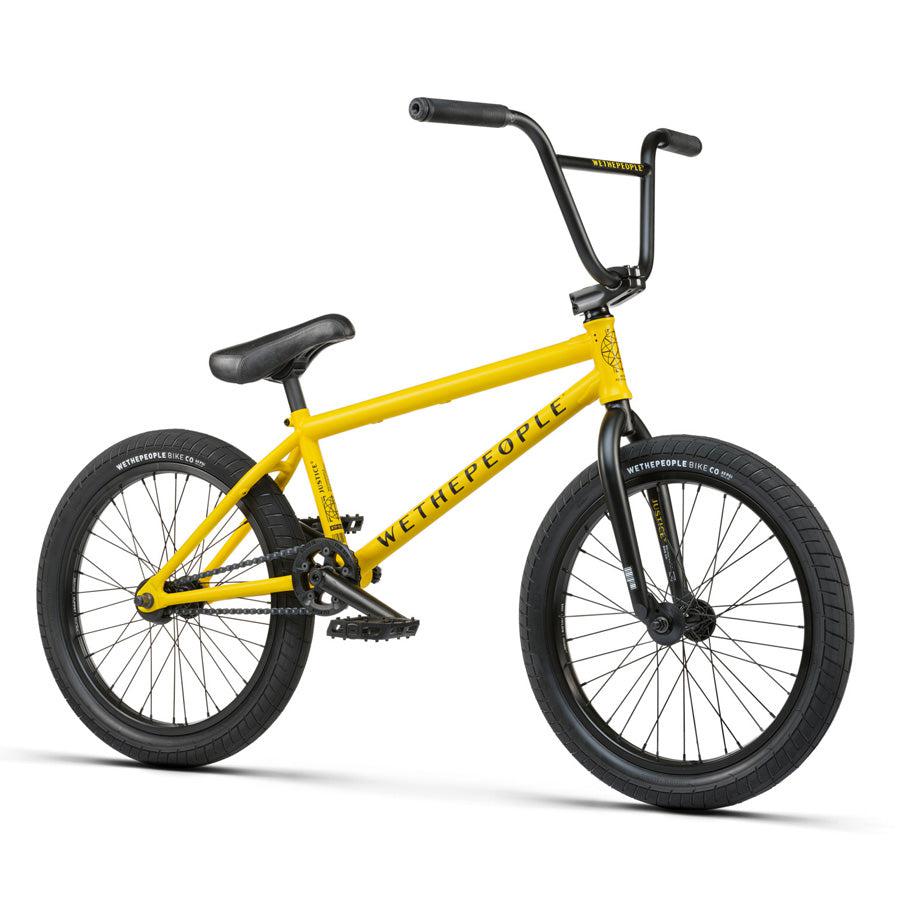 A yellow Wethepeople Justice 20 Inch Bike with top-of-the-line BMX components, featuring black handlebars, black tires, and a black seat.