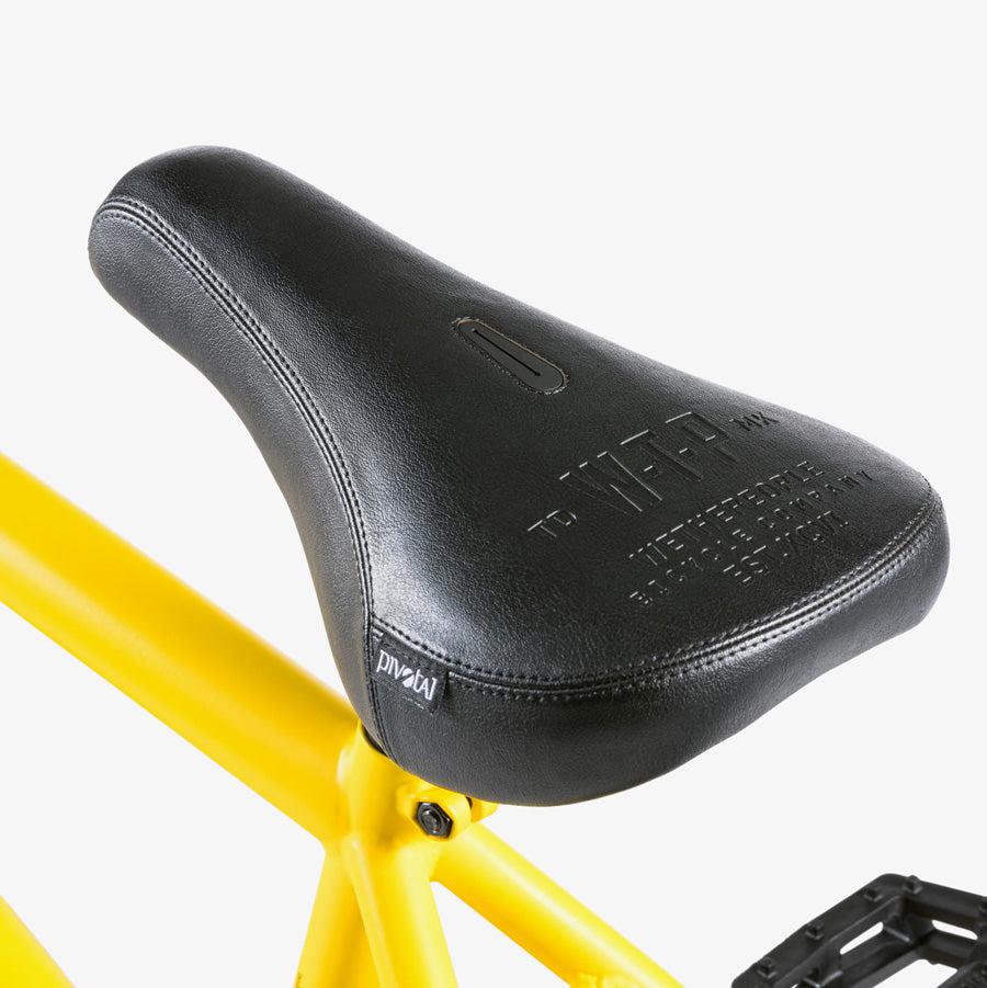 Close-up of a black bicycle seat mounted on a yellow bike frame, featuring embossed text and a small white label on the side. This Wethepeople Justice 20 Inch Bike showcases top-of-the-line BMX components for urban riders.