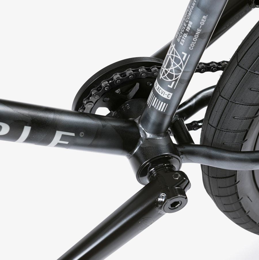 Close-up view of a top-of-the-line BMX crankset, chain, and rear tire on the black Wethepeople Justice 20 Inch Bike frame featuring a white geometric design and text.