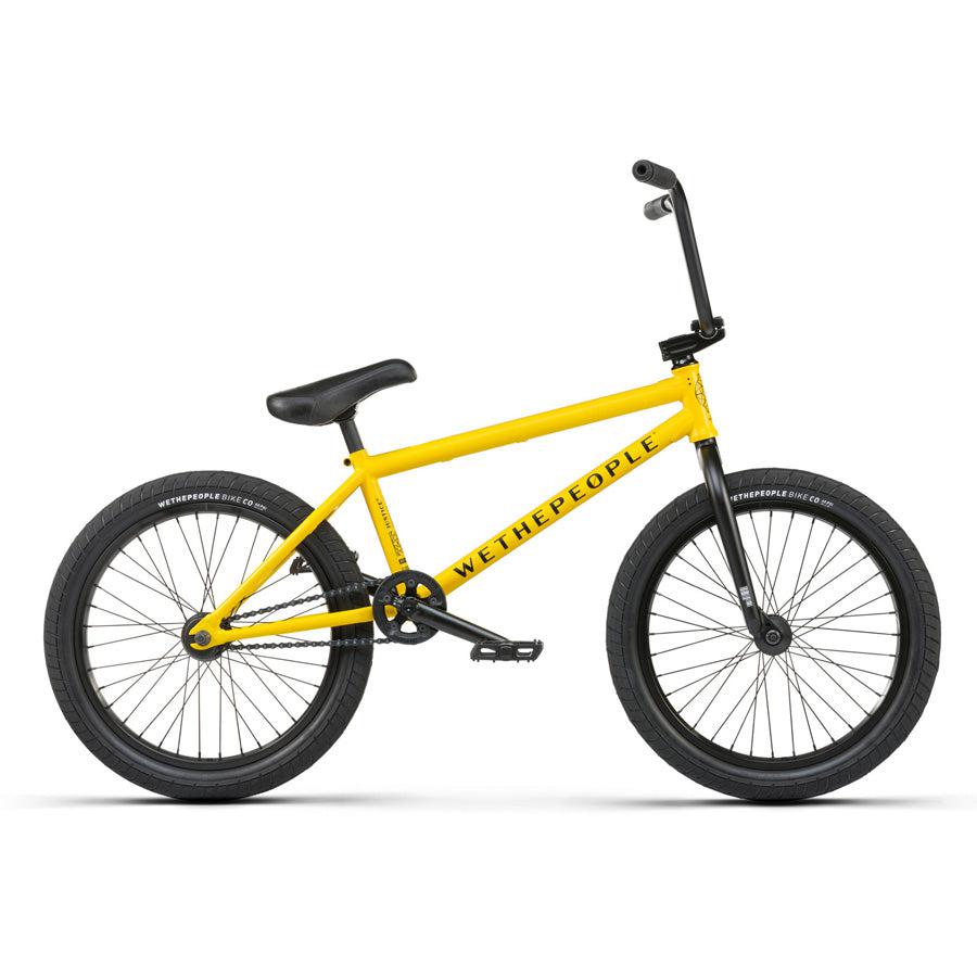 A yellow Wethepeople Justice 20 Inch Bike with black tires, a black seat, and black handlebars. The frame prominently displays "WETHEPEOPLE." This urban BMX bike features top-of-the-line components for an unparalleled riding experience.