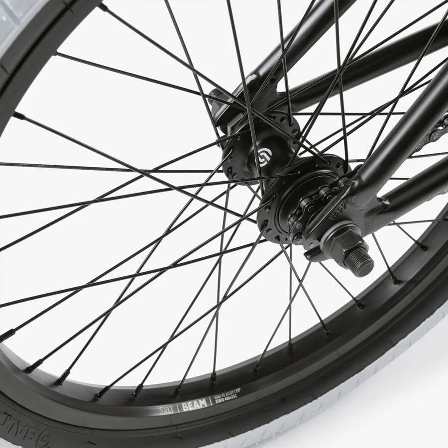 Close-up of a black BMX bike wheel with spokes, hub, and tire against a light background, showcasing the quality craftsmanship of the Wethepeople Nova 20 Inch Bike design for exceptional performance and style.