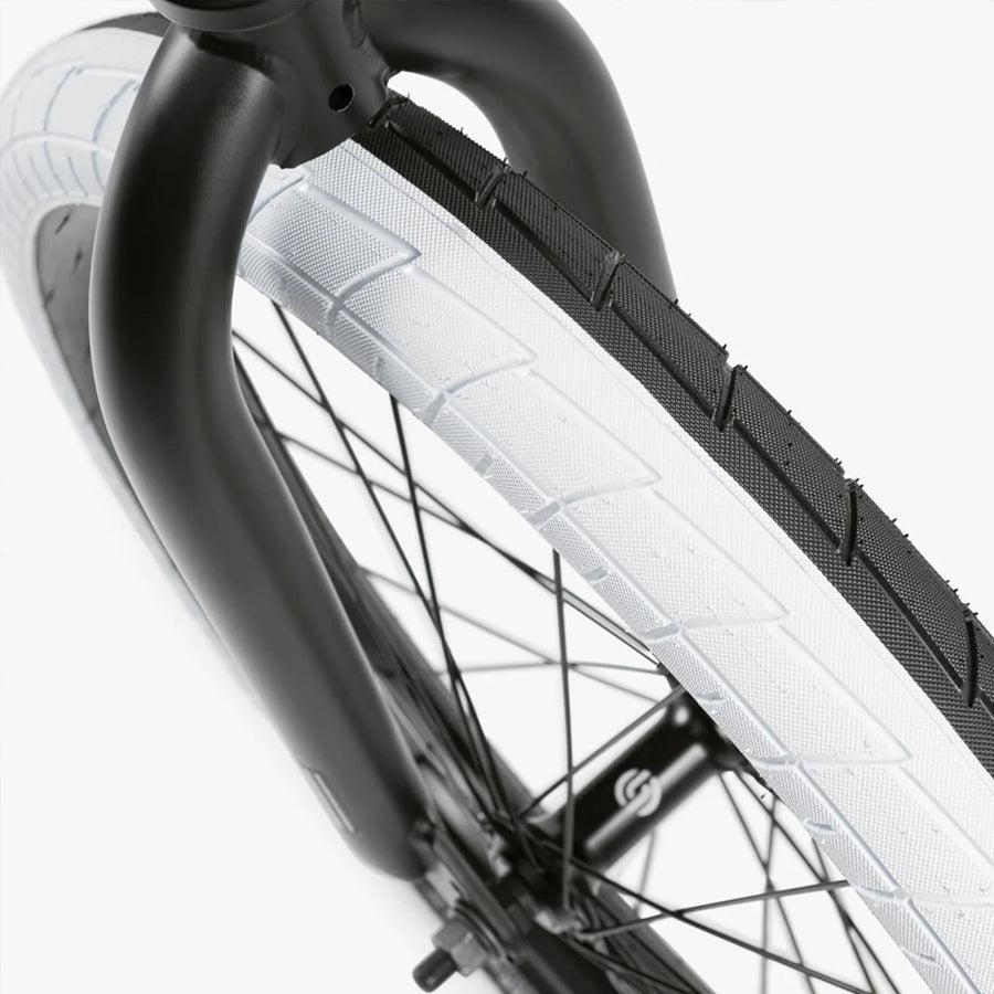 Close-up of a black bicycle fork and white tire with tread, showing the spokes and rim on a Wethepeople Nova 20 Inch Bike.