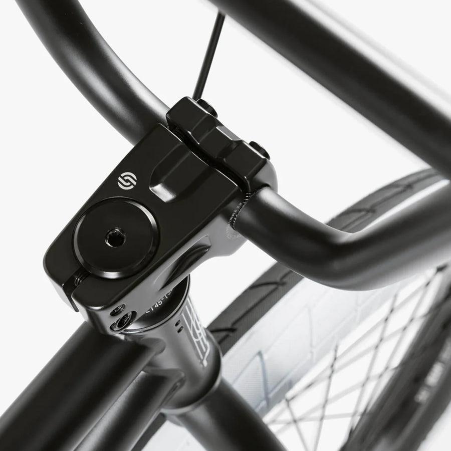 Close-up of a black BMX bike handlebar and stem against a white background, with a tire in the lower part. Its sleek design hints at top-quality components like the Wethepeople Nova 20 Inch Bike, ready to tackle any ride with confidence.
.
