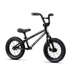 Black Wethepeople Prime 12 Inch Balance Bike featuring thick tires, a padded seat, straight handlebars, and "We The People" branding on the frame, shown from the side against a white background.