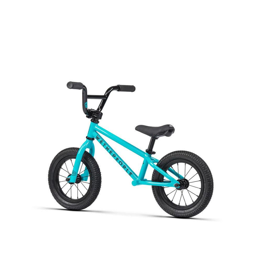 The Wethepeople Prime 12 Inch Balance Bike is shown in turquoise with black handlebars, seat, and wheels against a plain white background.