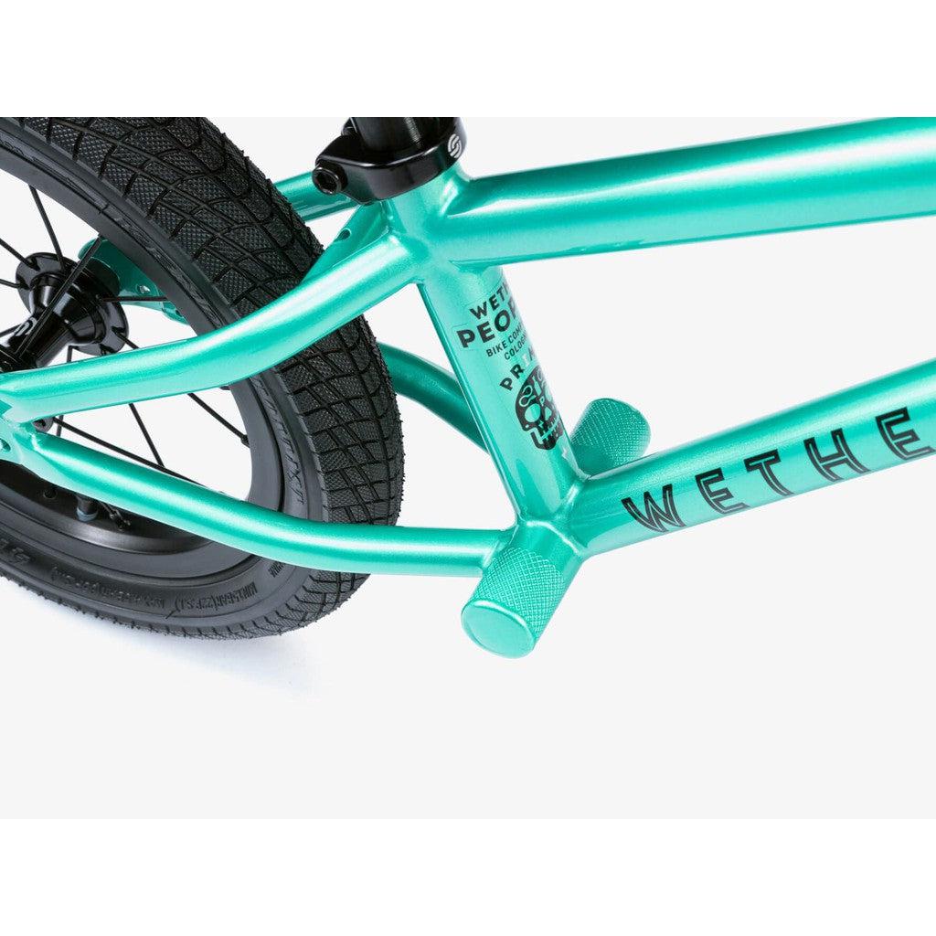 Close-up of a turquoise Wethepeople Prime 12 Inch Balance Bike frame featuring the rear tire, axle peg, and part of the WETHEPEOPLE logo.