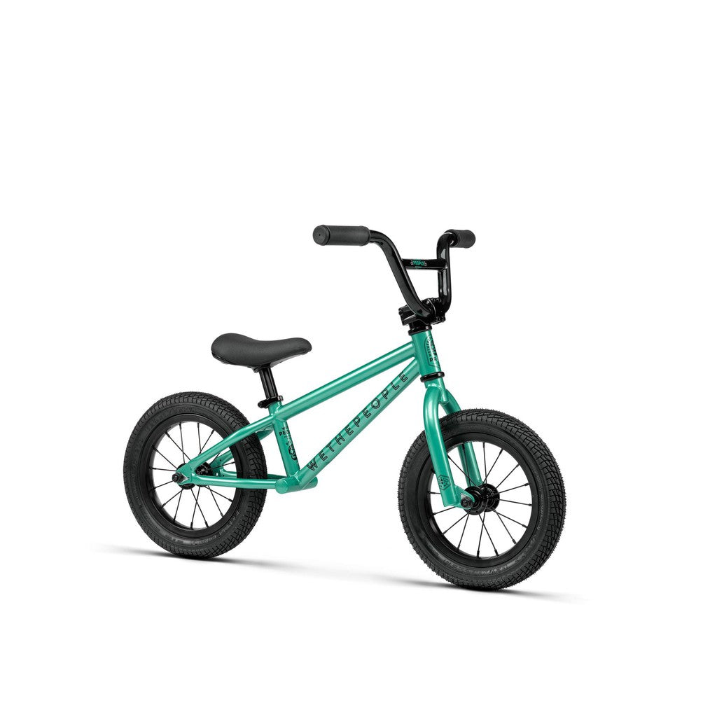 The Wethepeople Prime 12 Inch Balance Bike, shown in small teal with black handlebars, seat, and tires, is designed for young children and displayed against a white background.