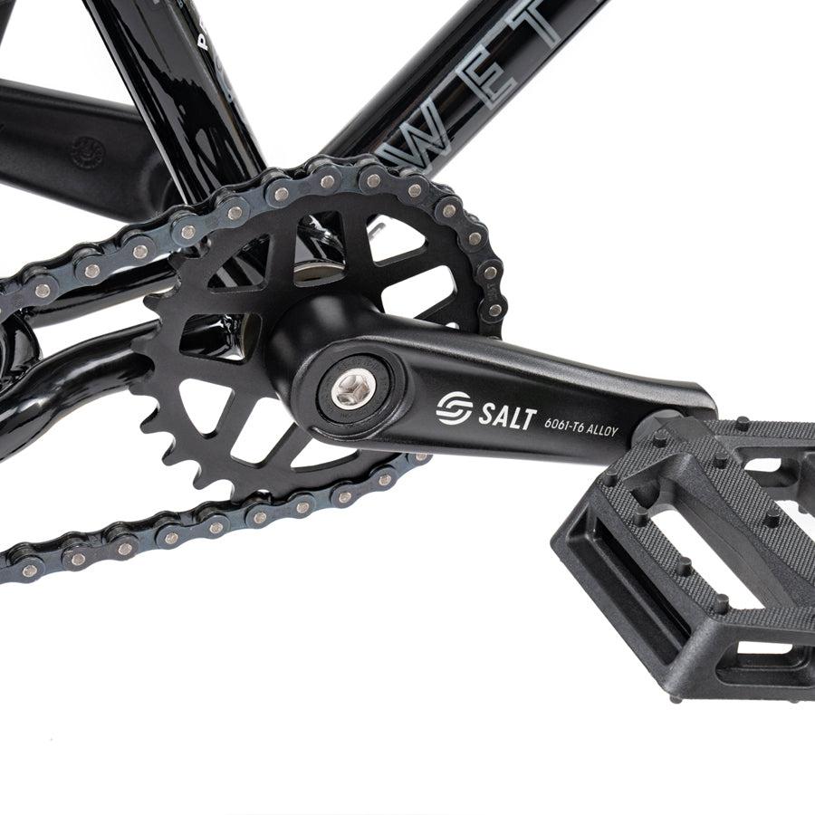 The Wethepeople Prime Drive 12 Inch Bike is equipped with a drivetrain, featuring a chain attached to it.