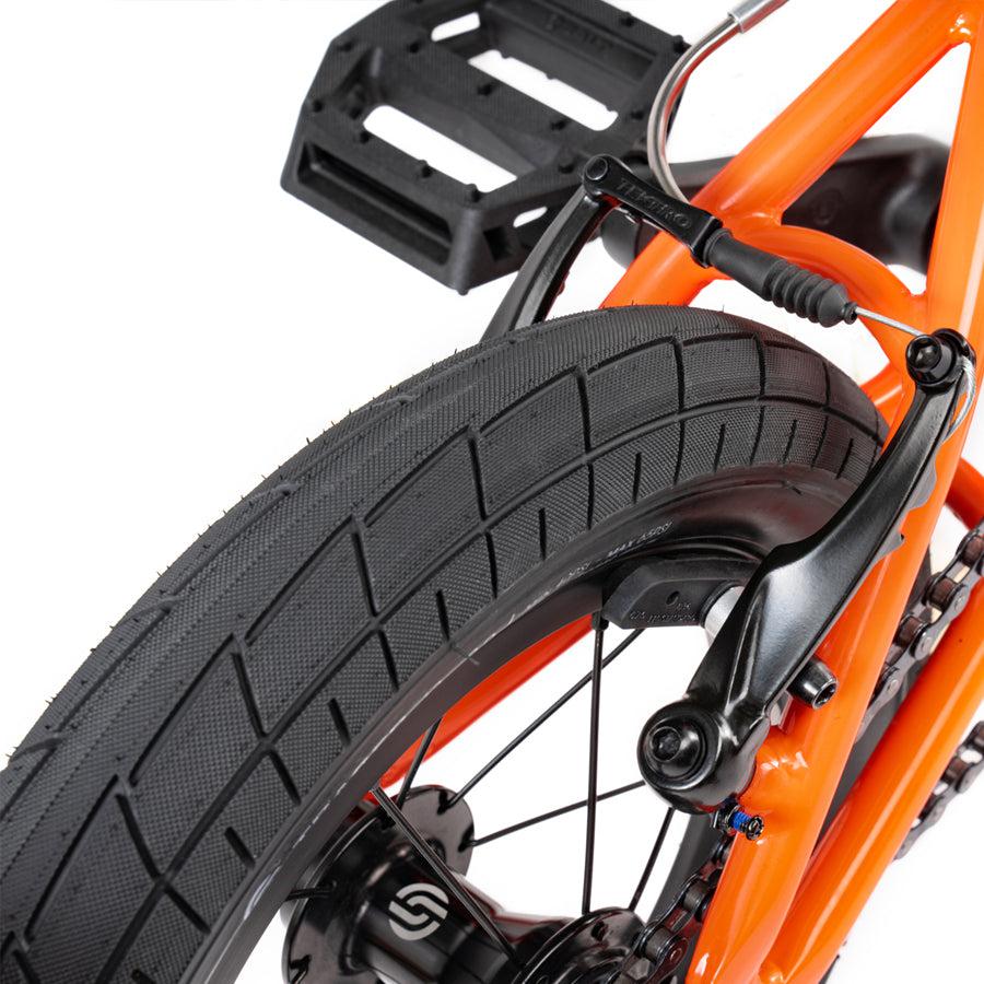 A close up of a Wethepeople Prime Drive 12 Inch Bike orange bicycle with a black tire.
